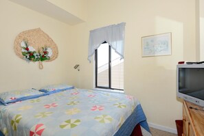 Un dormitorio con cama, televisor, ventana con vistas y un adorno en la pared.