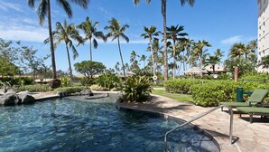 A clear pool with a diving board, surrounded by palm trees and greenery, indicating a resort setting.