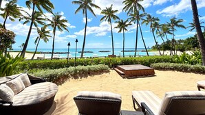 A beachside lounge with wicker furniture, a wooden deck, and a view of the ocean and palm trees.
