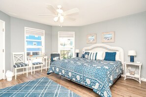 A bedroom with a bed, a desk, a chair, a window, and a ceiling fan.