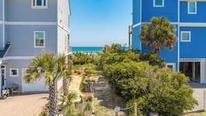 A beachfront property with a pathway leading to the ocean, surrounded by lush greenery and palm trees. - Boca North - Ocean View 3BR Home & Community Pool!!! (North Topsail Beach)