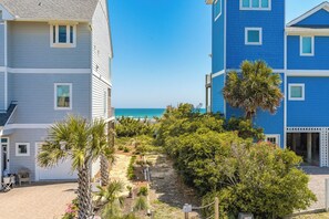 A beachfront property with a pathway leading to the ocean, surrounded by lush greenery and palm trees.