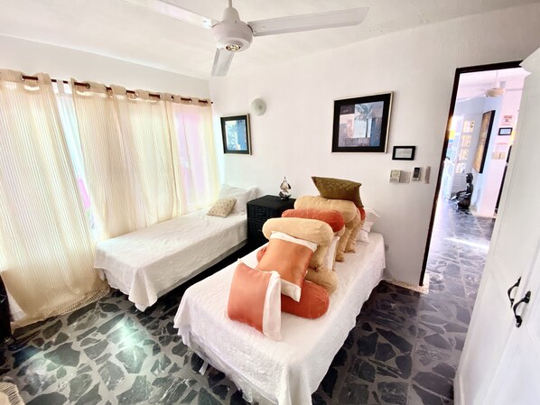 A room with two single beds, a ceiling fan, a small statue, and a door leading to another room.