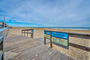 A wooden boardwalk leading to a beach with signs indicating beach access and no smoking rules.