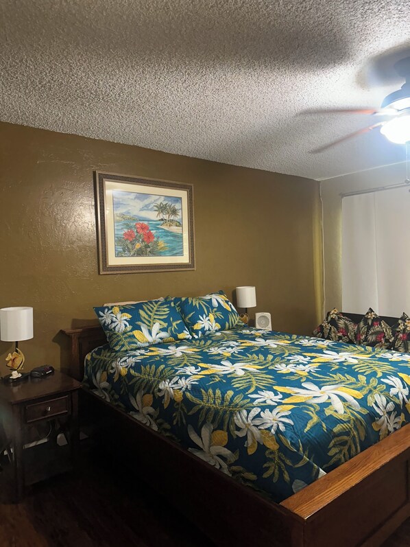 Une chambre à coucher comprenant un lit, une table de chevet, une lampe, un tableau encadré au mur et un ventilateur de plafond.