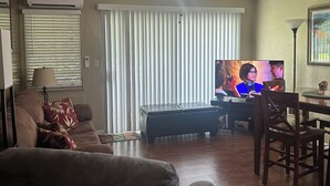 Un salon équipé d’un ventilateur de plafond, d’une télévision, d’un canapé, d’une table basse et d’une table à manger avec des chaises.