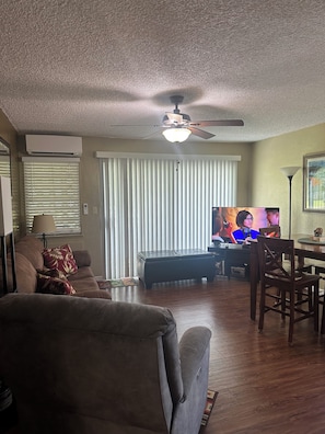 Una sala de estar con ventilador de techo, televisor, sofá, mesa de centro y una mesa de comedor con sillas.