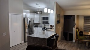 Una cocina moderna con armarios blancos, un refrigerador de acero inoxidable y una encimera de granito.