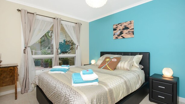 A bedroom with a bed, a bedside table, a nightstand, and a window with curtains.