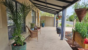 A covered patio area with potted plants, wicker furniture, and a concrete floor.
