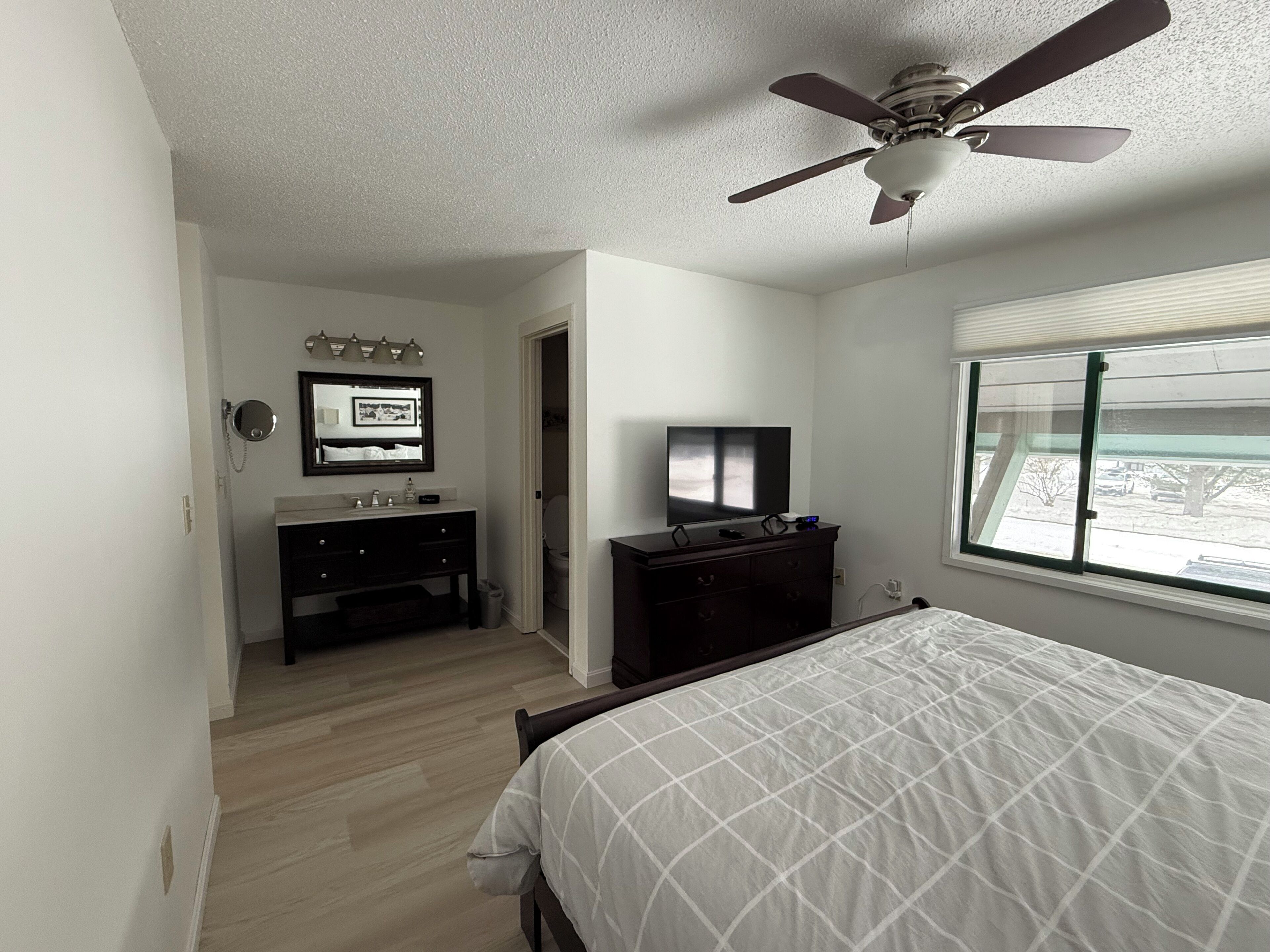 Ein Schlafzimmer mit Bett, Kommode, Fernseher, Deckenventilator und einem Fenster mit Blick.