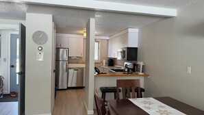 Una cocina compacta con electrodomésticos modernos, un comedor con mesa de madera y un reloj en la pared.