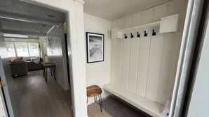 Un interior moderno con suelo de madera, una zona de estar con sofá y mesa, y un pasillo que conduce a una habitación con un gran ventanal.