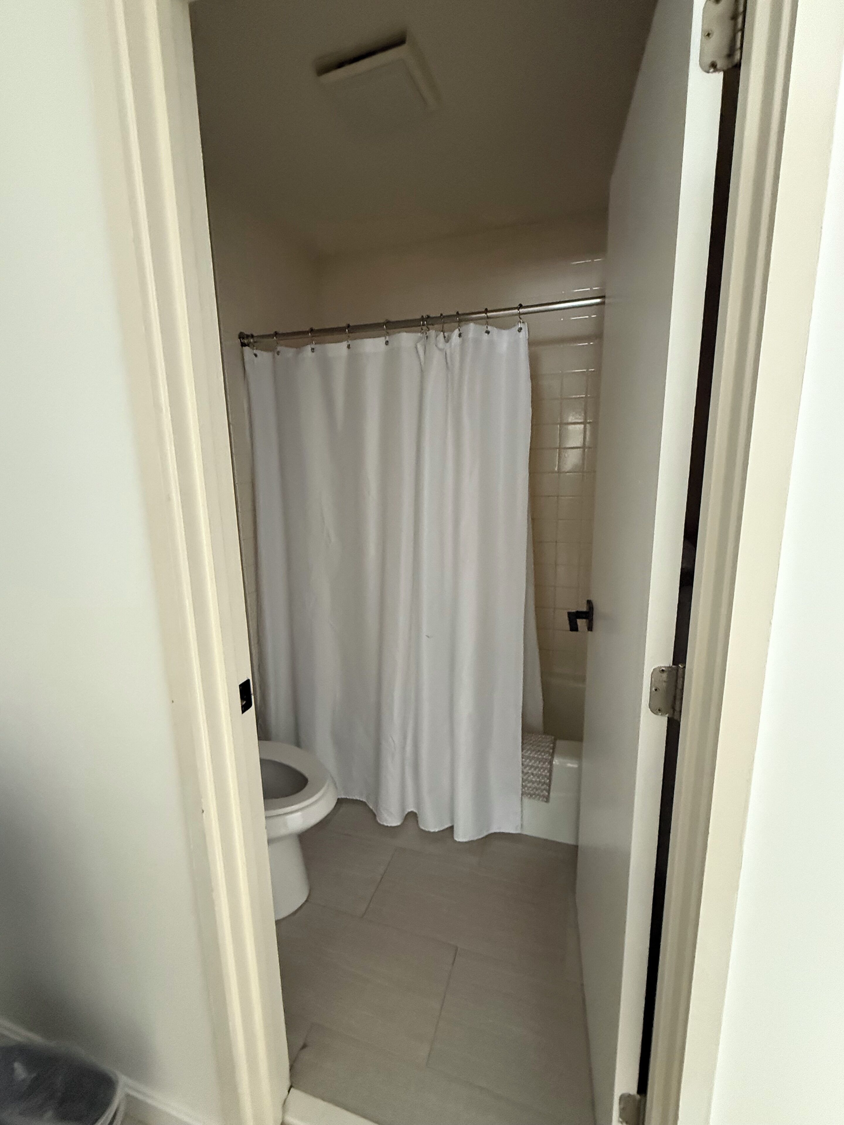 A small, white bathroom with a toilet, a shower, and a curtain.