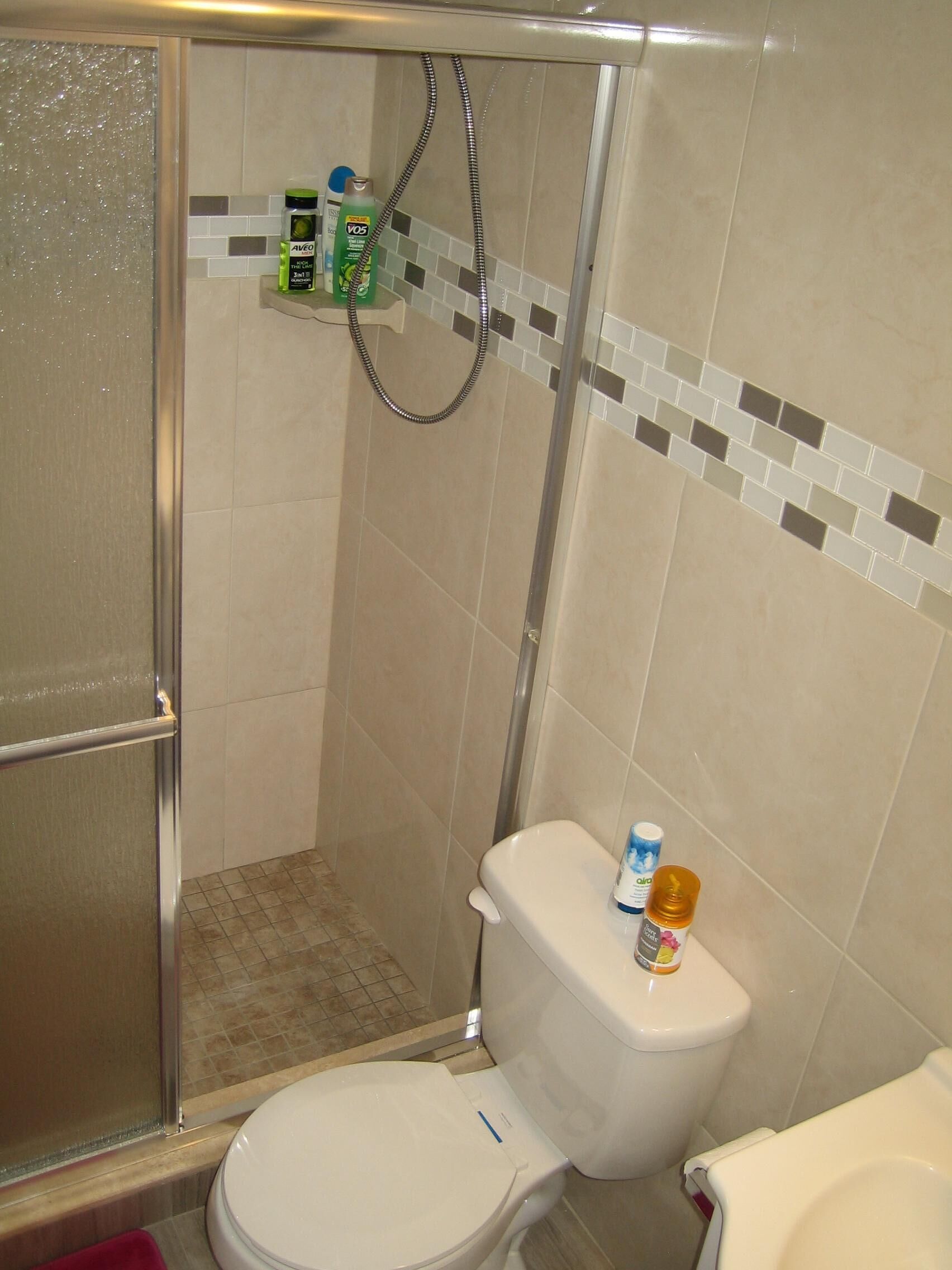 Une salle de bain équipée d’une douche, de toilettes et d’une étagère où sont rangés les articles de toilette.