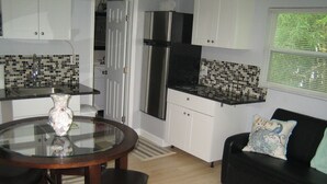 A compact kitchen with a dining area, a black sofa with a decorative pillow, and a window with blinds. - Private guesthouse near the beach (Sarasota)