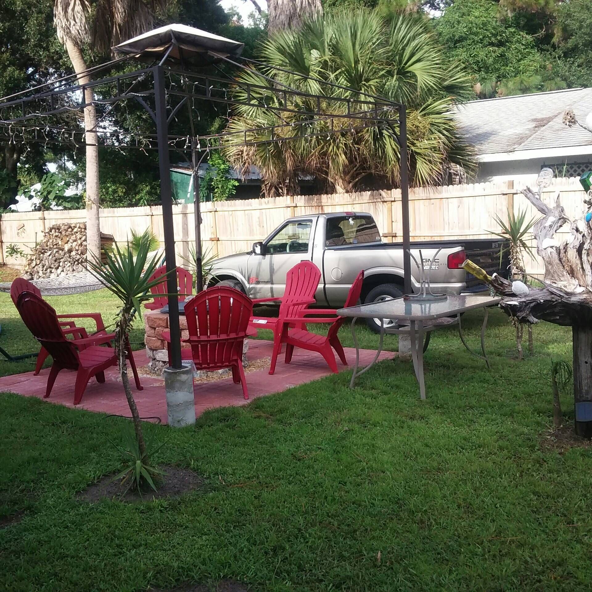 A backyard with a patio area, red chairs, a small table, and a parked truck.