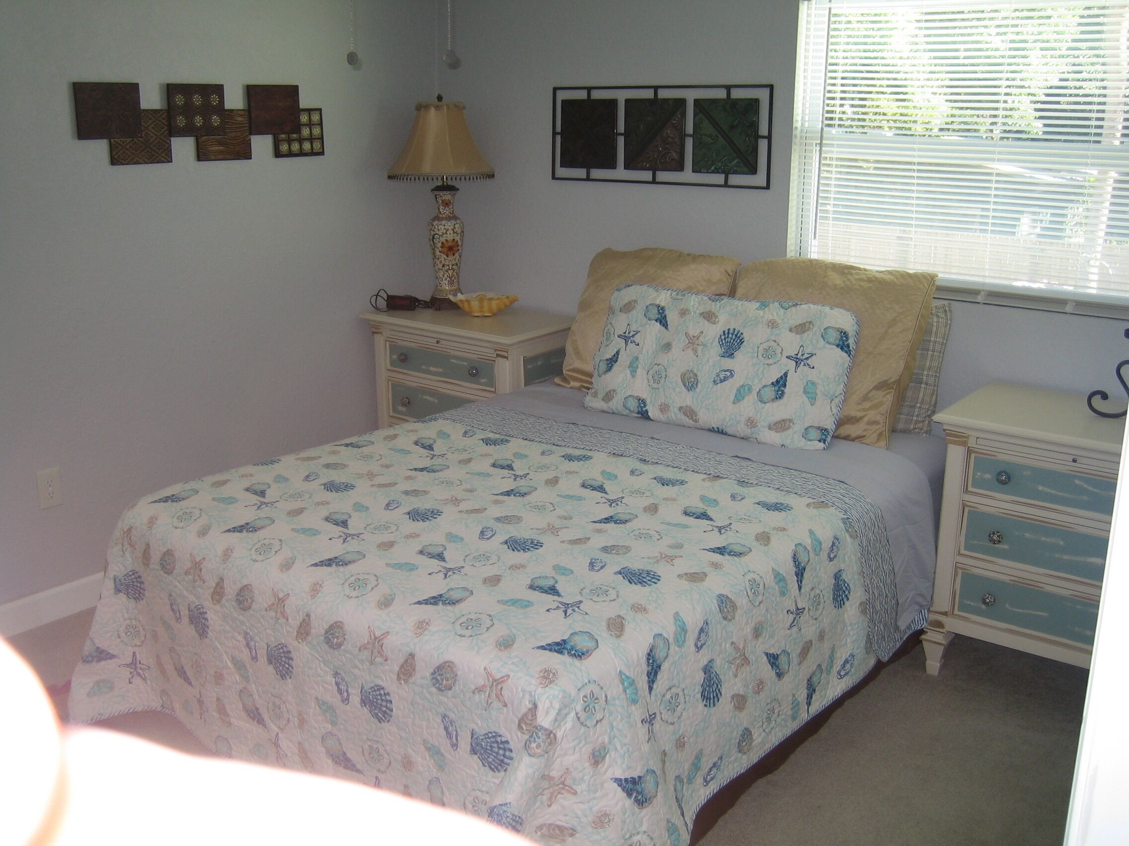 Un dormitorio con cama, mesitas de noche, lámpara y decoración en la pared.