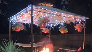A covered outdoor seating area with a fire pit, red chairs, hanging flower pots, and string lights. - Private guesthouse near the beach (Sarasota)