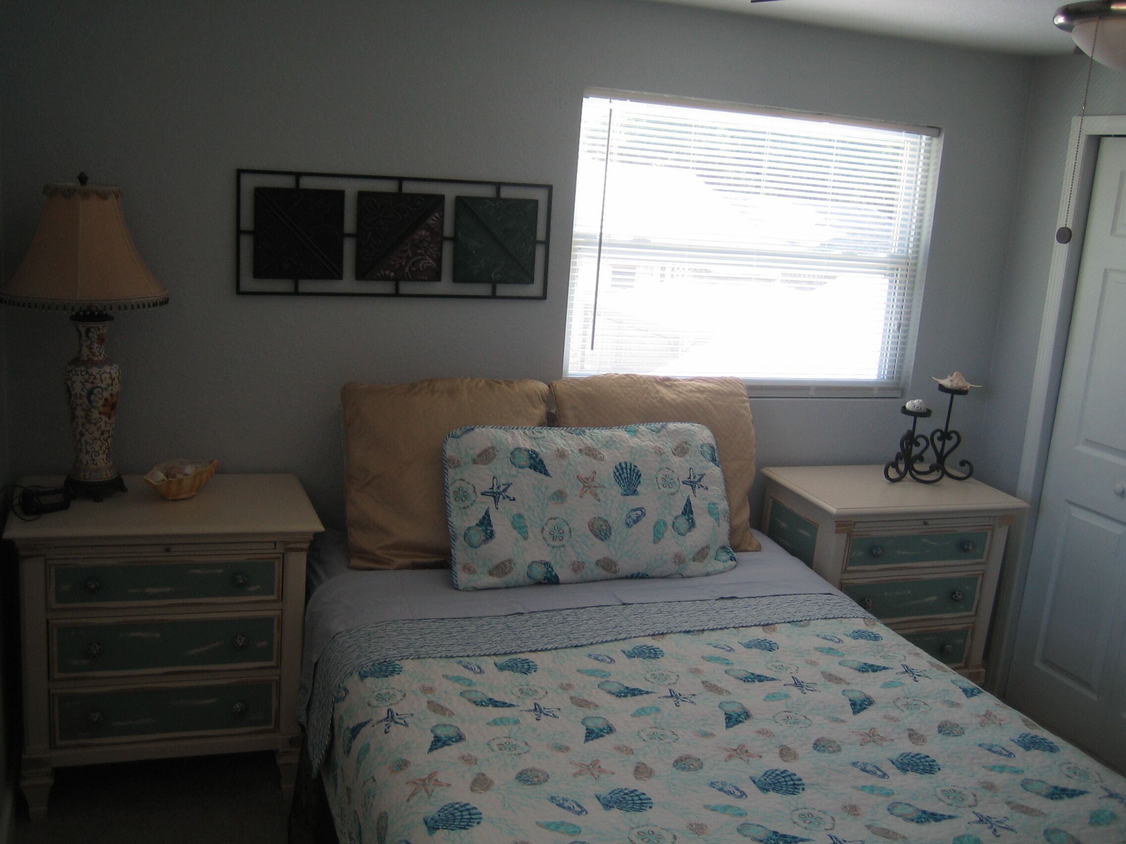 A bedroom with a bed, two nightstands, a lamp, and a window with blinds.