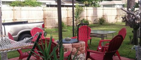 A backyard with a hammock, red chairs, a table, and a grill.