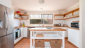 A modern kitchen with a central island, stainless steel appliances, and wooden shelves. - Casa Moana - views of the beach (Gerringong)