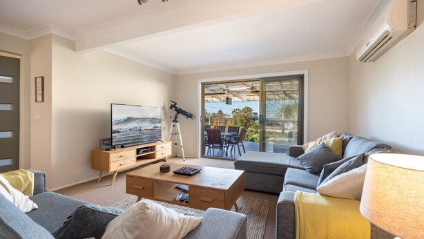 A modern living room with a flat-screen TV, a telescope, and a balcony with outdoor furniture. - Casa Moana - views of the beach (Gerringong)