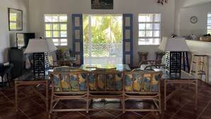 A spacious dining area with a high ceiling and large windows, a dining table with chairs, and a view of the outdoors.