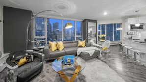 A modern living room with a city view, grey sofas, a glass coffee table, and a kitchen area with white cabinets. - Stunning modern luxury 2 bedroom, 2 bath condo rental  (Vancouver)