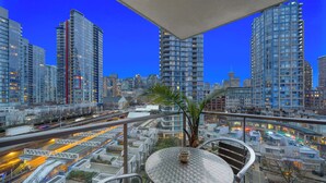 A high-rise building with a glass facade, a balcony with a round table and chairs, and a cityscape view in the background. - Stunning modern luxury 2 bedroom, 2 bath condo rental  (Vancouver)