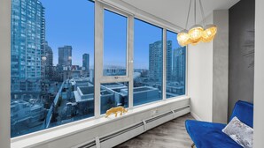 A modern room with large windows, a blue sofa, and a city view. - Stunning modern luxury 2 bedroom, 2 bath condo rental  (Vancouver)