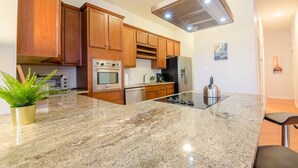 A modern kitchen with wooden cabinets, a stainless steel range hood, a built-in oven, a refrigerator, and a granite countertop. - Rustic Red - 2Bd 2 Bath in a Historic Brick 1913 (Atlanta)