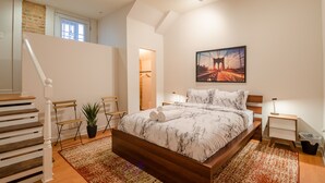 A bedroom with a wooden bed, a nightstand, a potted plant, and a staircase. - Rustic Red - 2Bd 2 Bath in a Historic Brick 1913 (Atlanta)