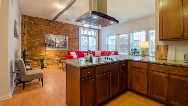 A kitchen with a large island, wooden cabinets, and a brick wall. - Rustic Red - 2Bd 2 Bath in a Historic Brick 1913 (Atlanta)