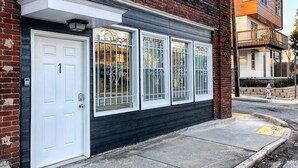A two-story residential building with a white door and three large windows with decorative metal grilles. - Rustic Red - 2Bd 2 Bath in a Historic Brick 1913 (Atlanta)