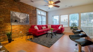 A living room with a red sofa, a glass coffee table, and a ceiling fan. - Rustic Red - 2Bd 2 Bath in a Historic Brick 1913 (Atlanta)