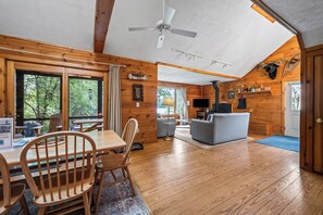 A wooden cabin interior with a dining area, a sofa, a television, and a ceiling fan.