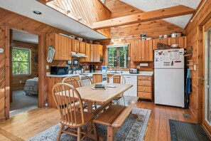 A wooden cabin kitchen with a dining table, chairs, and a refrigerator.