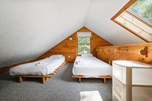 Een kleine, driehoekige slaapkamer op zolder met twee eenpersoonsbedden, een houten hoofdbord en een dakraam.