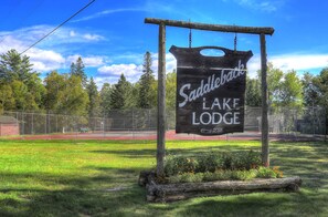 Schild für die Saddleback Lake Lodge mit einem eingezäunten Tennisplatz im Hintergrund.