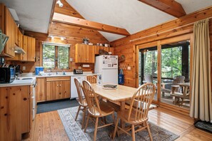 A wooden cabin interior with a kitchen, dining area, and large windows.