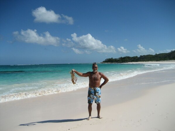 A person standing on a beach holding a camera, with clear blue water and a distant shoreline.