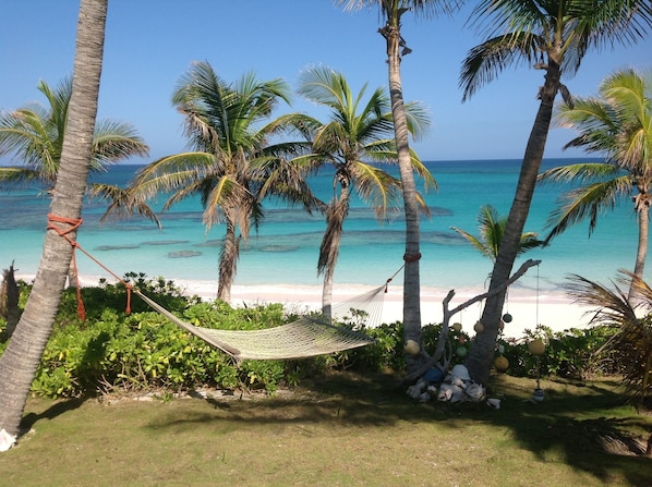 Una hamaca atada entre palmeras con vista a una playa y agua turquesa cristalina.
