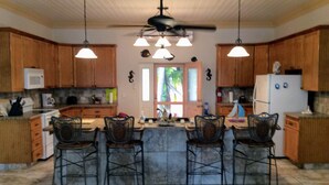 A spacious kitchen with wooden cabinets, a central island with bar stools, a ceiling fan, and pendant lighting. - Da Villa Ocean Front Home, Luxury & Privacy on Pink Sand Beach (Governor's Harbour, Eleuthera)