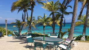 An outdoor seating area with a view of the ocean, surrounded by palm trees. - Da Villa Ocean Front Home, Luxury & Privacy on Pink Sand Beach (Governor's Harbour, Eleuthera)