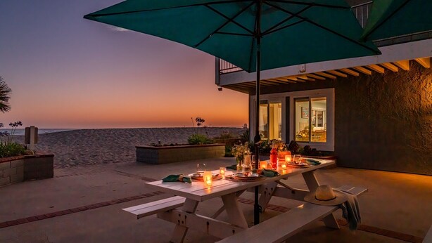 Vista do pôr do sol a partir de um pátio com mesa posta para dois, guarda-sol e vista para o oceano.
