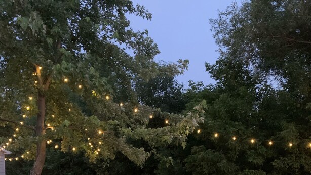 Ein Garten mit Feuerstelle, Picknicktischen und Lichterketten.