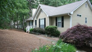 A two-story house with a front porch, a small garden with various plants, and a metal fence.