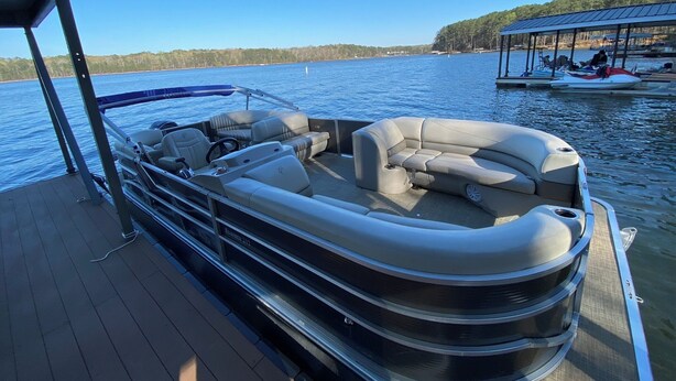 A pontoon boat with a covered seating area and a docked boat in the background.