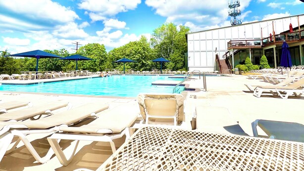 Un espace piscine avec des chaises longues et des parasols, un ciel dégagé et un bâtiment doté d’un balcon.